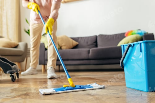 Cleaner mopping a hardwood living room floor with a flat microfibre mop and bucket