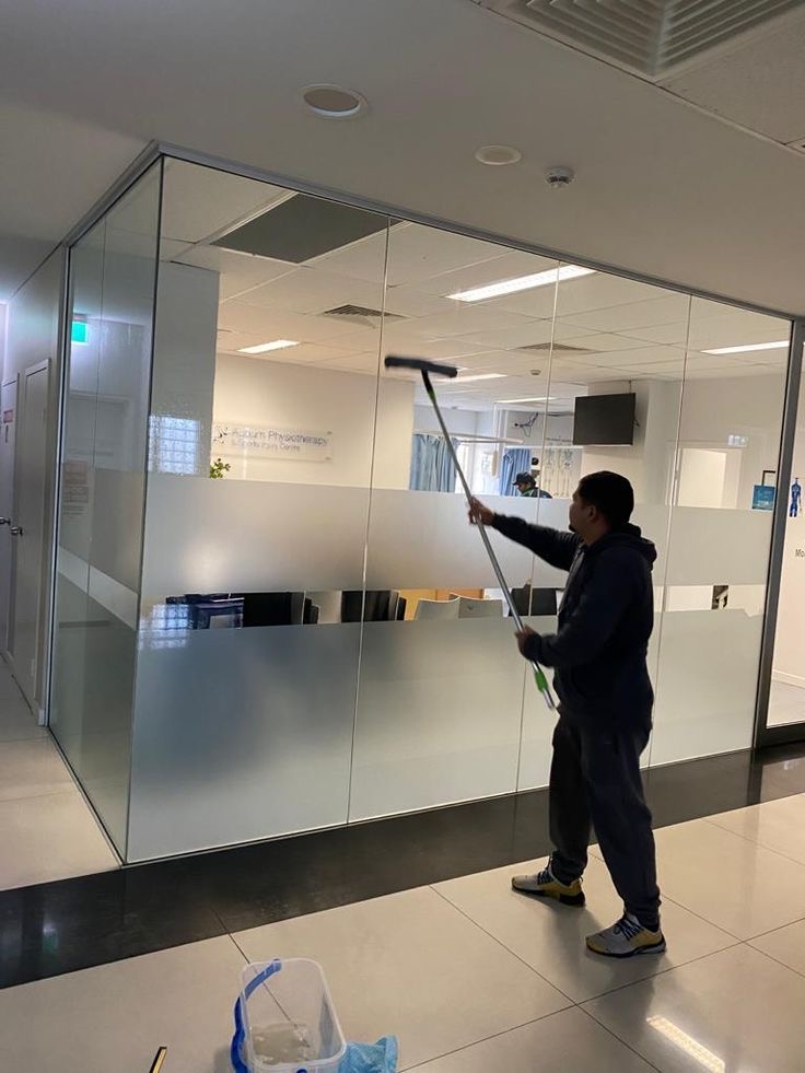 Technician washing tall glass office partitions with an extension pole