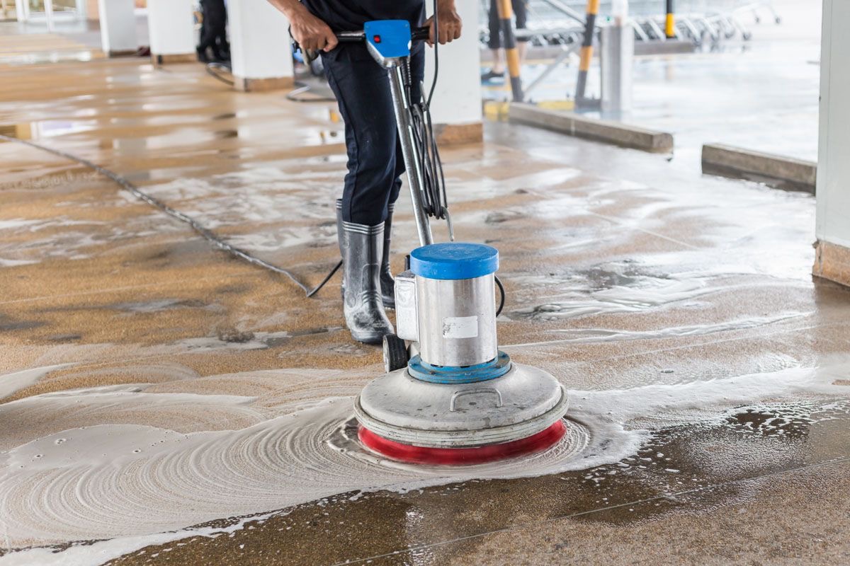Operator scrubbing a concrete floor with a rotary scrubber