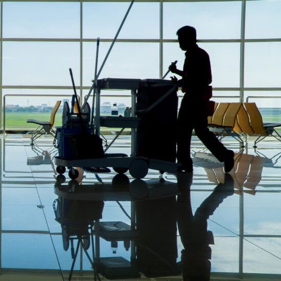 Day porter pushing a fully stocked janitorial cart across a polished concourse