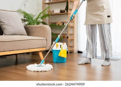 Cleaning technician mopping a hardwood floor beside a sofa